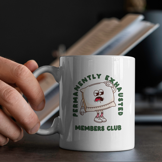 White mug with cartoon character and text held by a hand on a blurred background