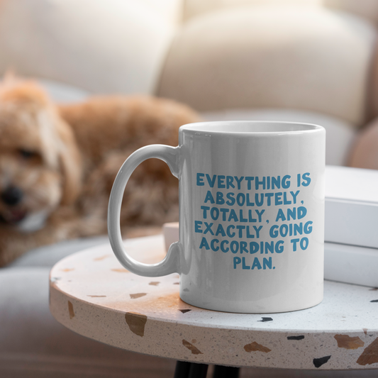 White mug with blue text on a small round table with a dog in the background
